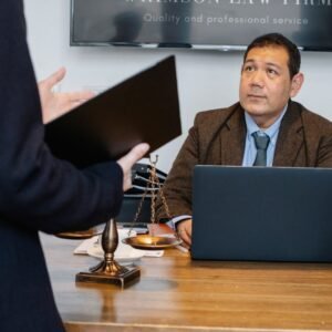 Crop unrecognizable employee representing new case details to concentrated middle aged ethnic lawyer sitting at table with laptop gavel and justice scales
