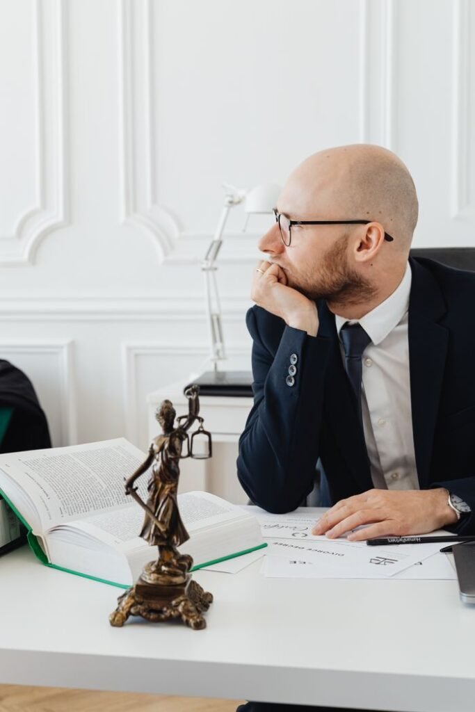 Lawyer in office with legal documents, deep in thought at desk with Temida statue.